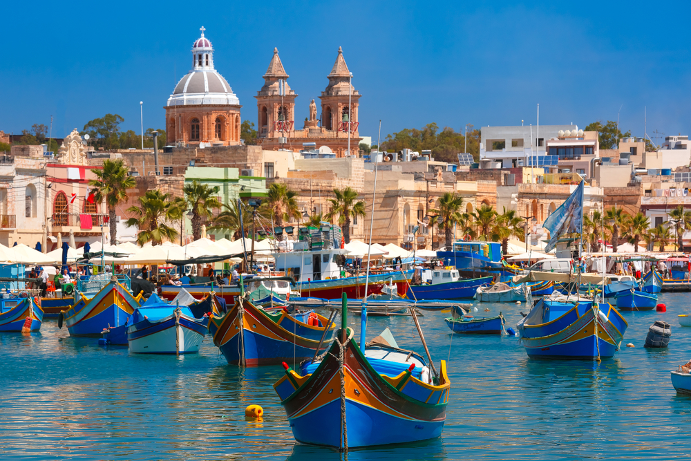 A kép a máltai Marsaxlokk halászfalu kikötőjét ábrázolja. A kikötő tele van hagyományos, élénk színű máltai halászhajókkal, amelyeket luzzu néven ismernek.  - Z(s)eppelin utazás